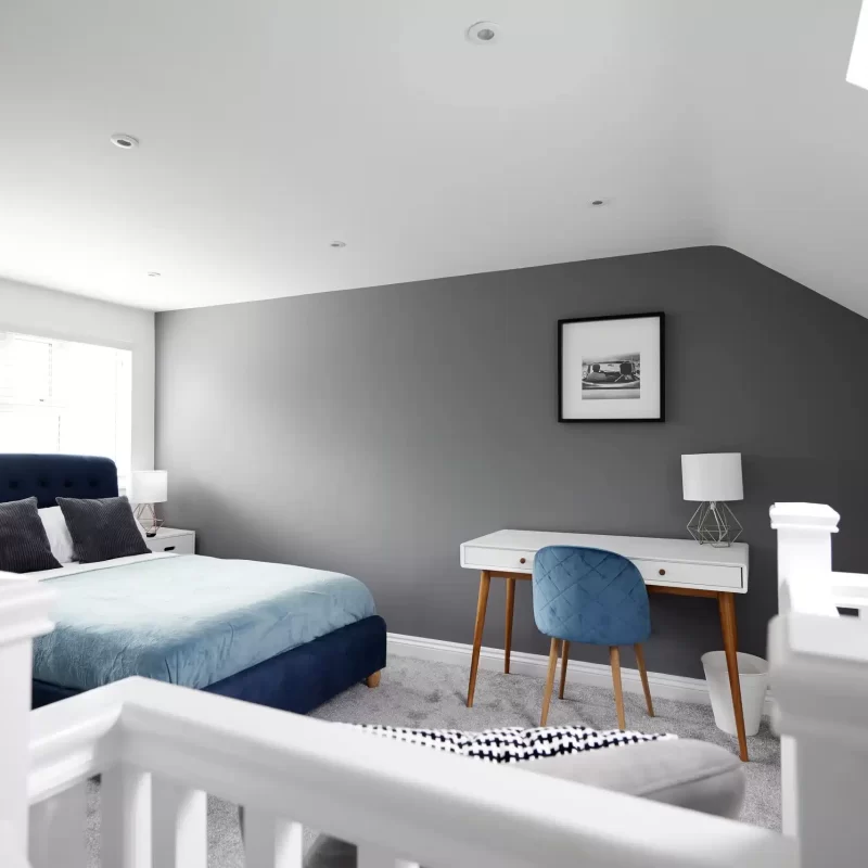 Bedroom finished in a deep grey and white with blue chair in a loft conversion by forest builders